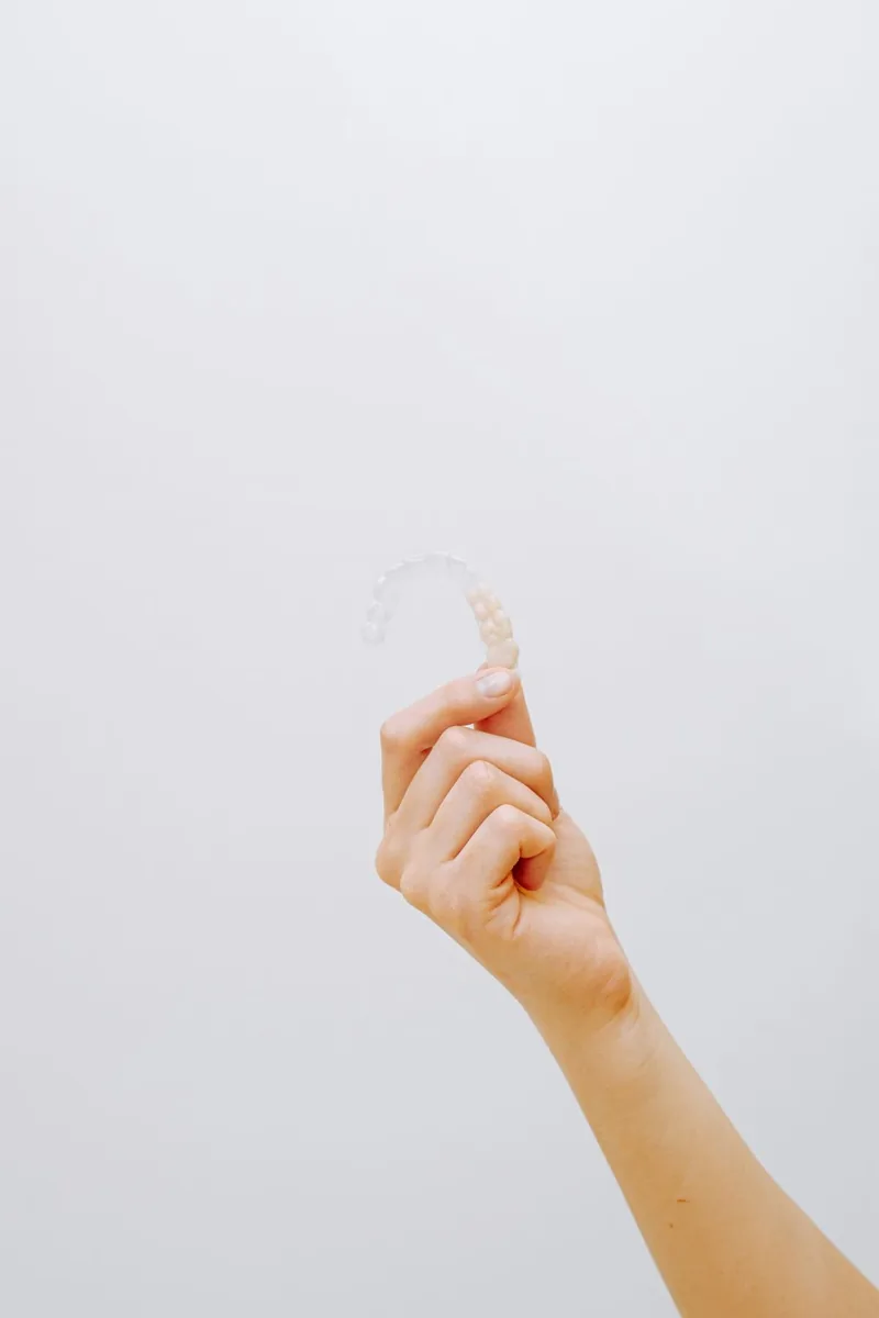 Illustrative photo of a hand holding a clear orthodontic aligner against a plain background