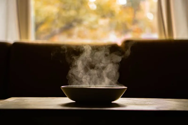 Illustrative photo of a bowl of warm soup steaming on a table by a window